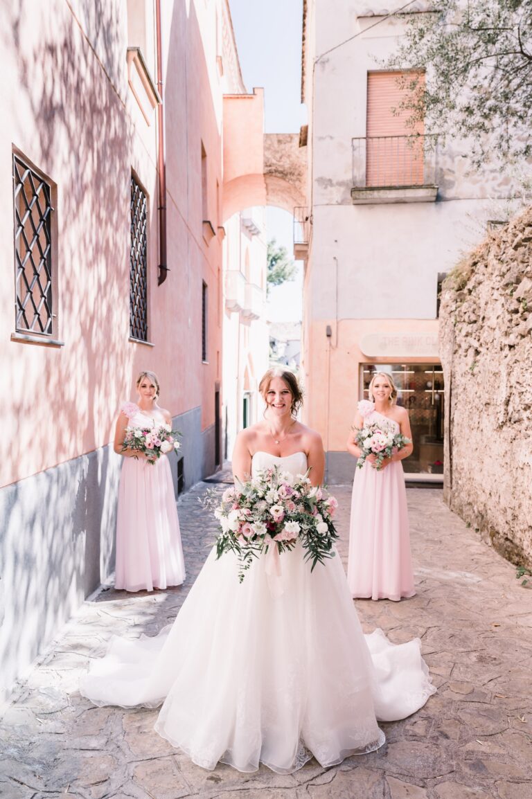 The bride and her bridesmaids in a narrow pink-walled lane, Mr and Mrs Wedding In Italy