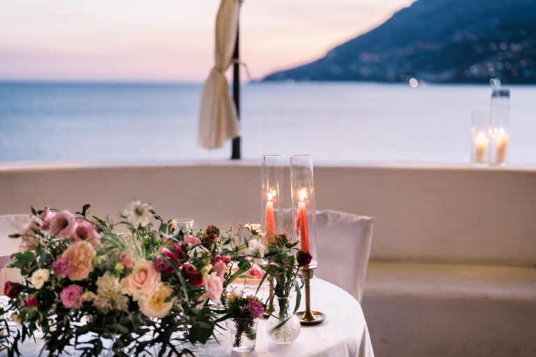 A table for two at dusk with garden roses and pink tapers, the sea and coastline beyond, Mr and Mrs Wedding In Italy