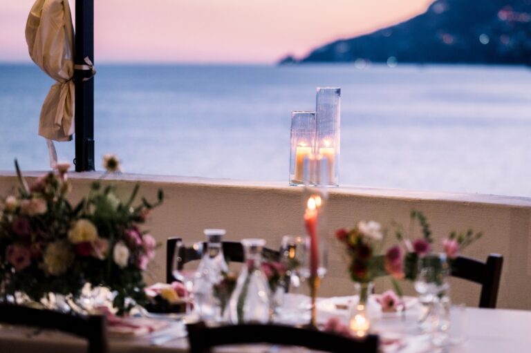 A terrace table at dusk, candles along its length and the coast going dark behind, Mr and Mrs Wedding In Italy