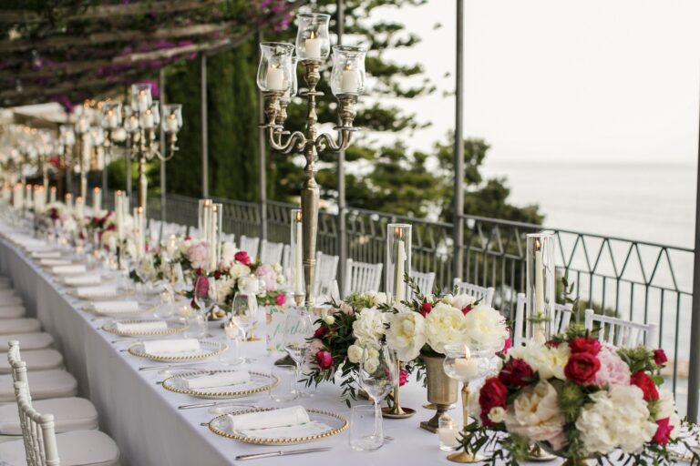 A long table on a terrace above the sea, candelabra and red and white flowers down the centre, Mr and Mrs Wedding In Italy