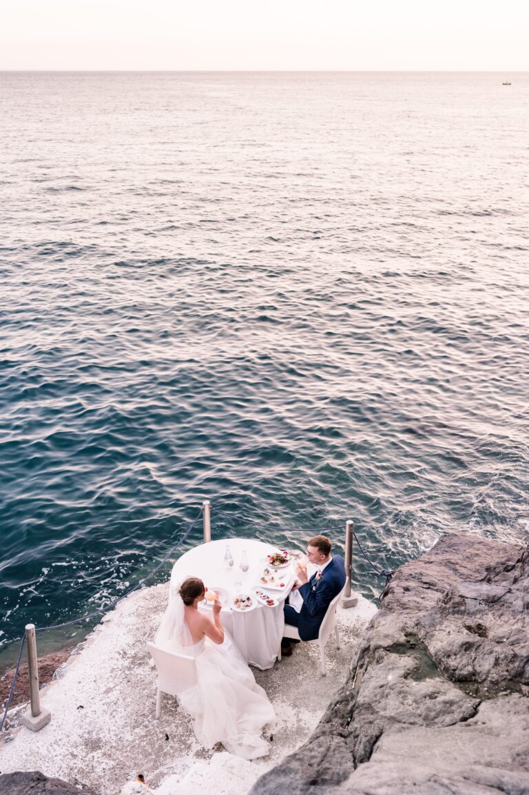 A table for two laid on the rocks at the water's edge, seen from above, Mr and Mrs Wedding In Italy