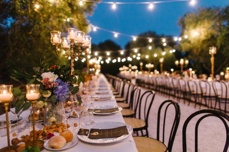 A long table under strings of lights at dusk, candelabra and gold-rimmed chairs, Mr and Mrs Wedding In Italy