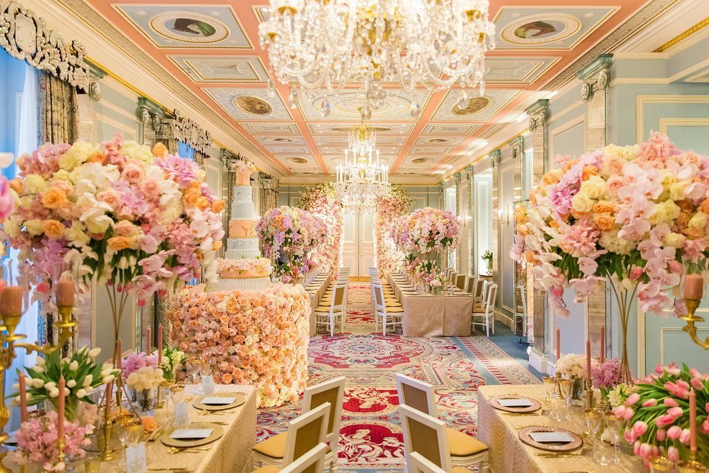 Long banqueted reception room with a chandelier, painted ceiling and tall pastel floral centrepieces, set for a wedding dinner., My Dubai Wedding Planner