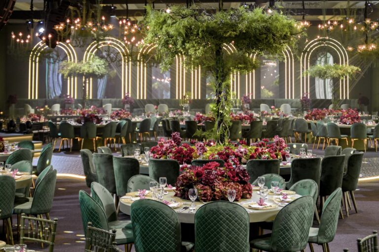Glasshouse-style hall with illuminated arches, a central living tree and green velvet chairs at dressed tables, MY Event Design