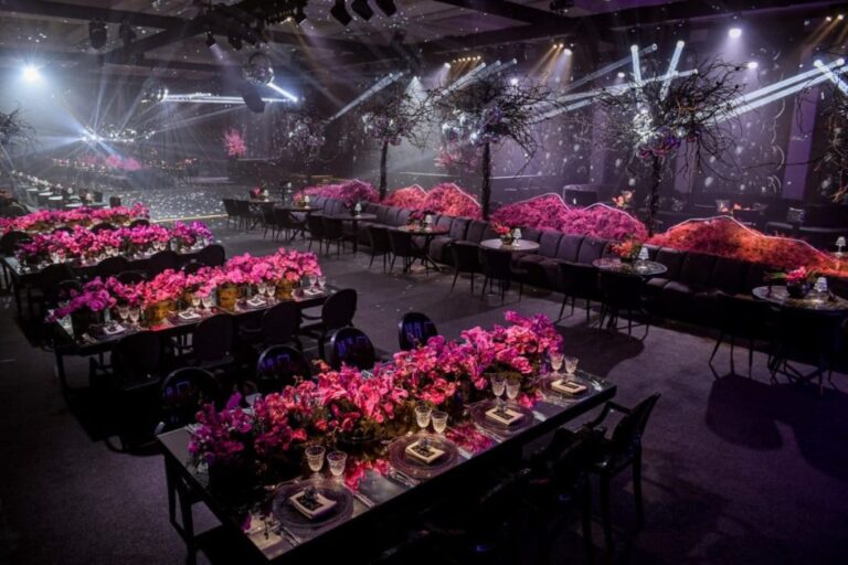 Long tables lined with magenta flowers in a darkened hall with stage lighting, MY Event Design