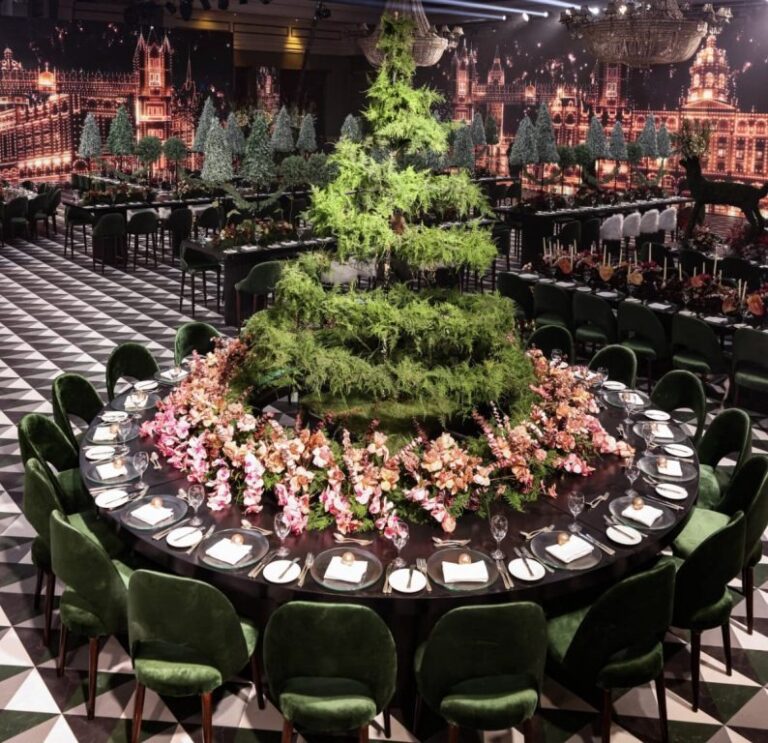 Large round table ringed with pink flowers and a clipped evergreen centrepiece on a monochrome tile floor, MY Event Design