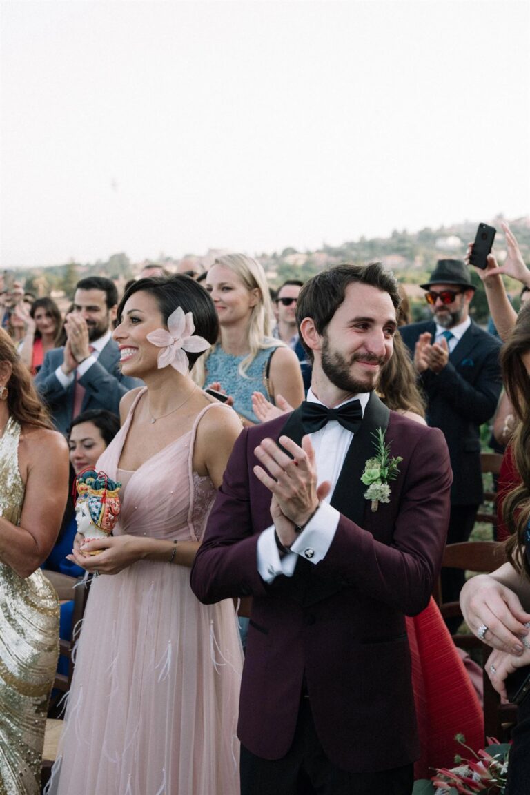Guests applaud during the ceremony, one holding a hand-painted Sicilian pupo doll dressed in its own miniature costume, My Sicilian Wedding