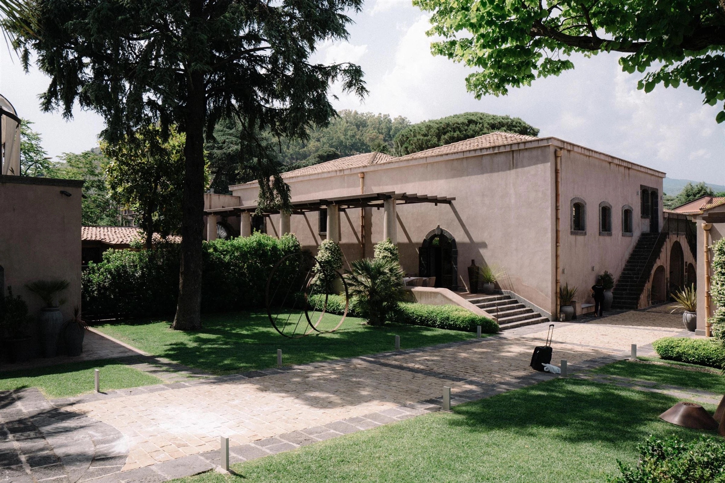 The venue's stone facade and tiled roof, reached along a cobbled drive beneath a wooden pergola and cypress trees, My Sicilian Wedding