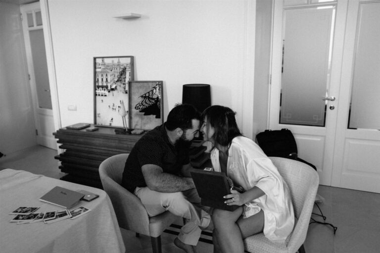The bride and groom lean forehead to forehead in a quiet moment, old photographs spread on the table beside them, My Sicilian Wedding