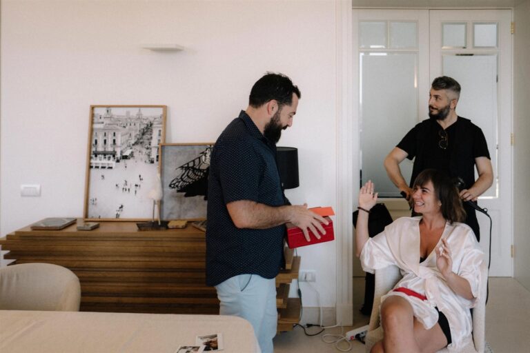 The groom adjusts his braces before a mirror as his best man ties a bow tie nearby, My Sicilian Wedding