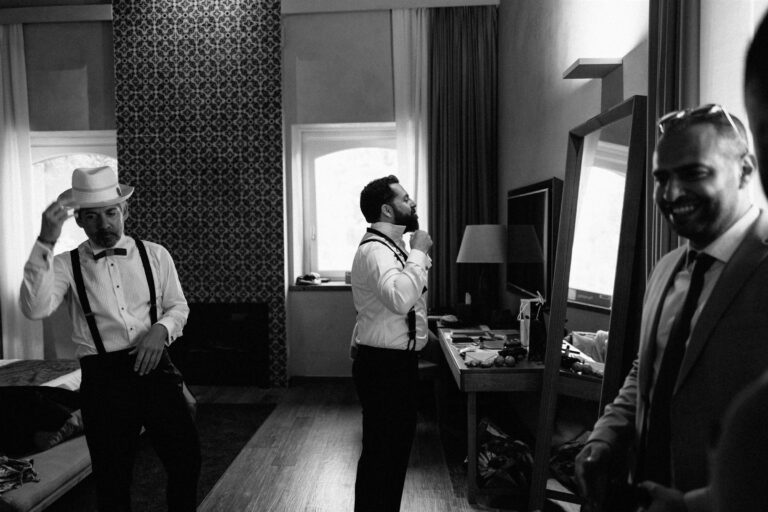 Groomsmen in braces and bow ties get ready together, one settling a straw fedora onto his head, My Sicilian Wedding