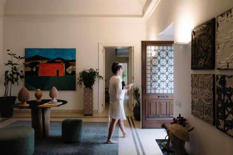 The bride, in her robe with a tiara already pinned, crosses an elegant hallway hung with Sicilian folk art, My Sicilian Wedding
