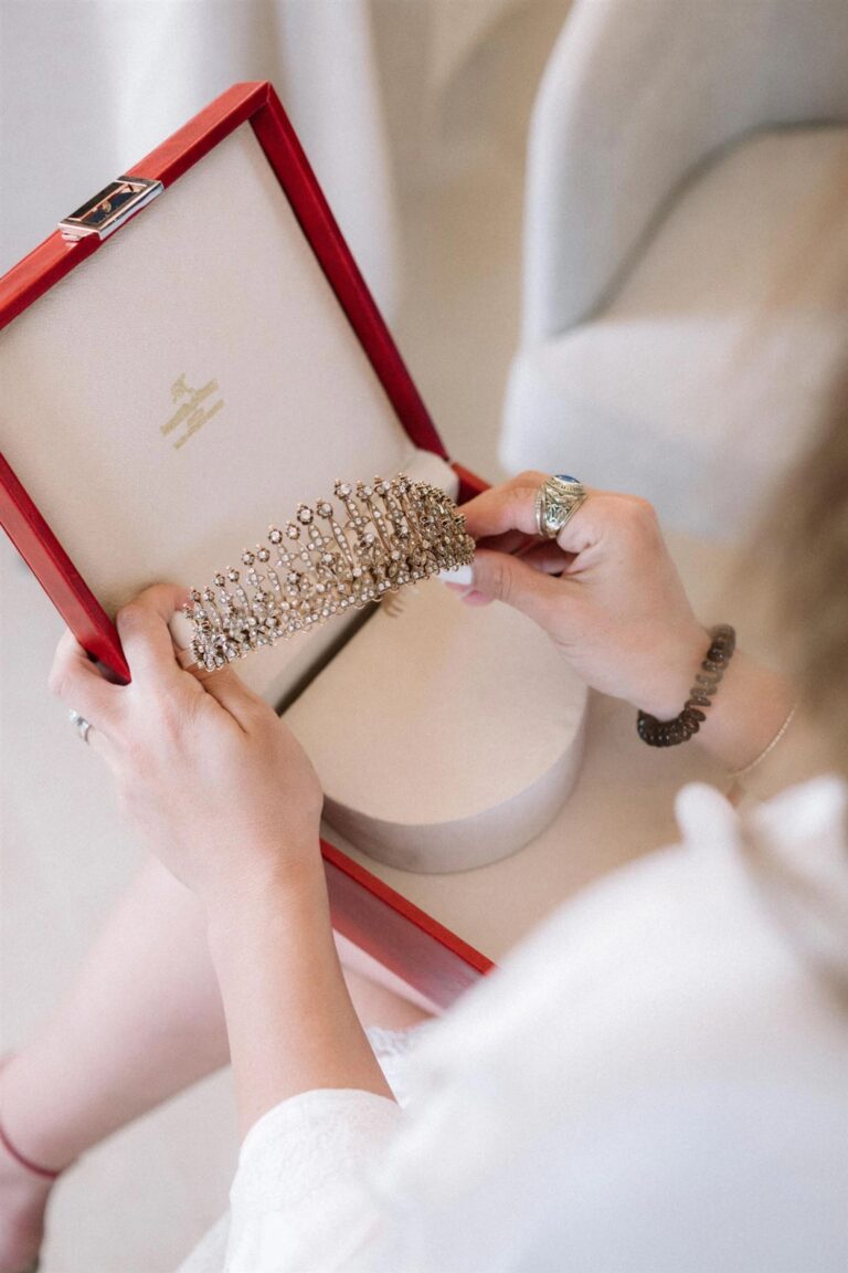 A bridal tiara is lifted from its red presentation box, the bride's rings visible on her hands, My Sicilian Wedding
