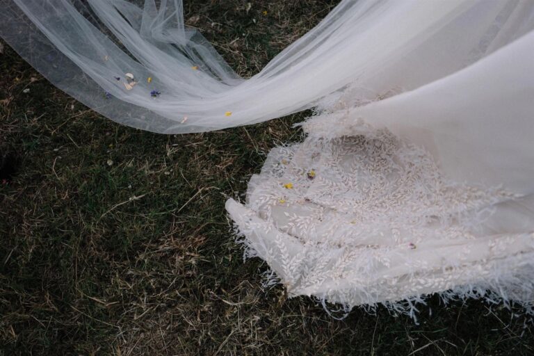 The bride's veil and the lace, feather-trimmed hem of her gown lie spread across the grass, My Sicilian Wedding
