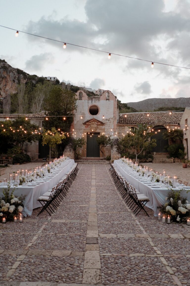 Two candlelit tables running to a chapel with a round window, lights strung above, My Sicily Wedding