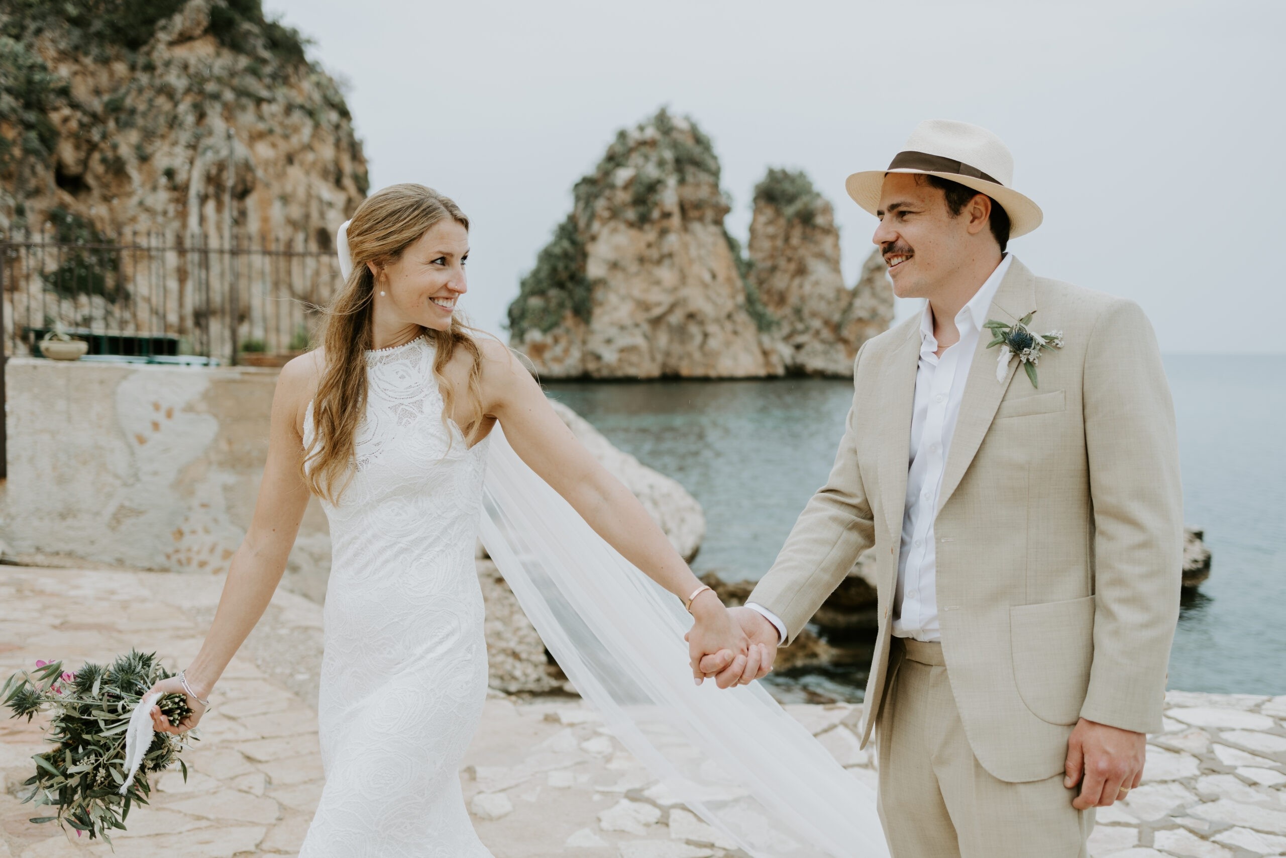 Hand in hand on the tonnara cobbles, the sea stacks at Scopello behind them, My Sicily Wedding