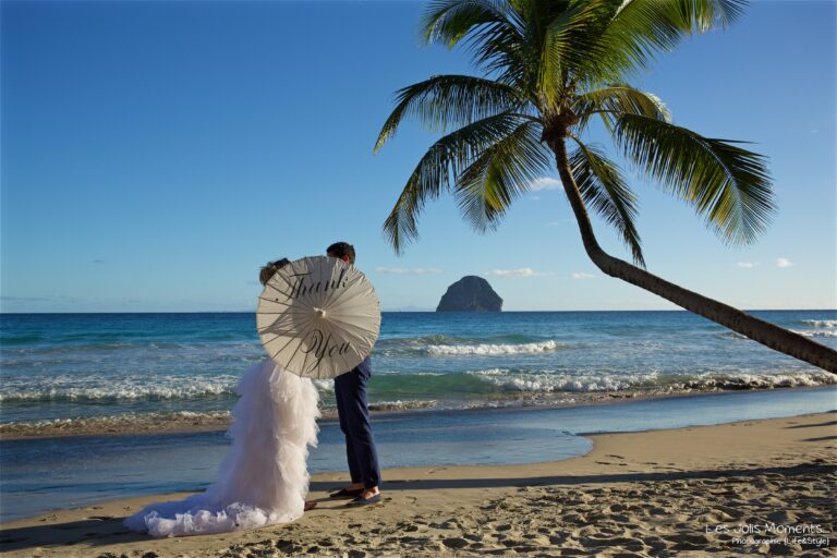 A couple under a lace parasol on a Martinique beach, with Diamond Rock rising from the sea behind them, Myl'Evasions