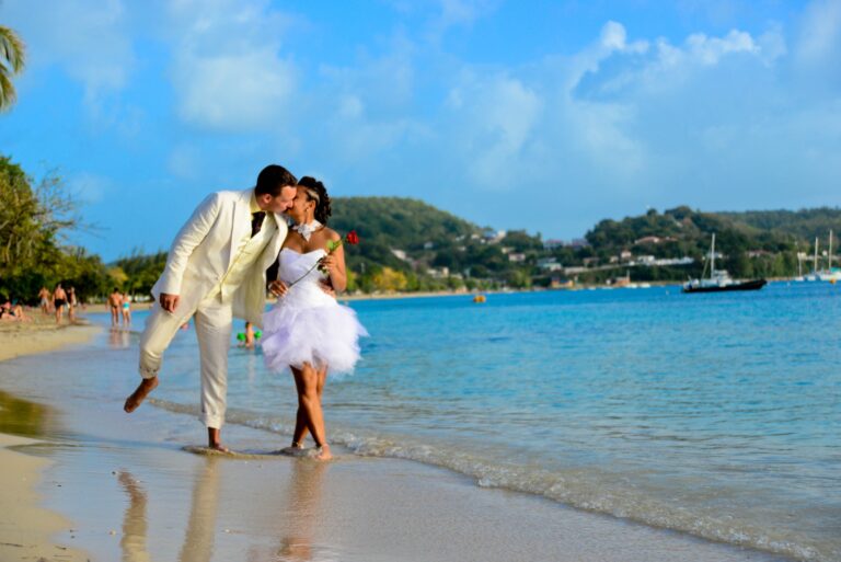 A bride and groom in white kissing in the shallows of a calm bay, Myl'Evasions