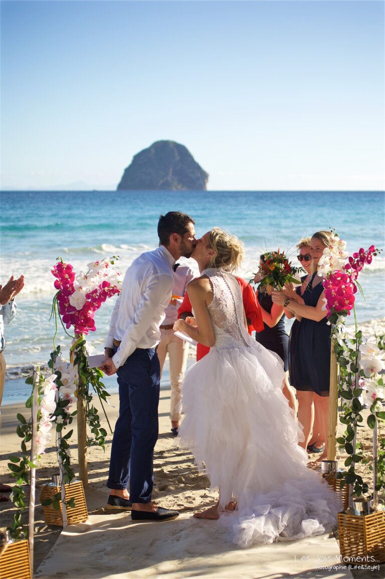 A couple at the end of a flower-edged beach aisle with Diamond Rock behind, Myl'Evasions