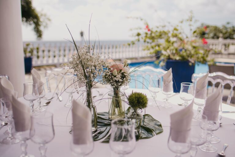 A dining table with small flower arrangements and folded napkins, set above a sea-view terrace, Myl'Evasions