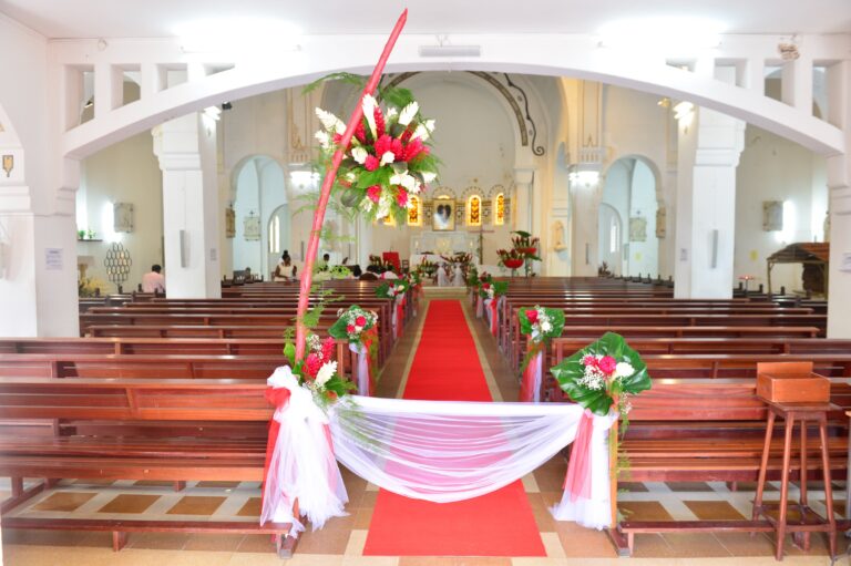 A church nave with a red carpet aisle dressed with flowers and draped fabric, Myl'Evasions