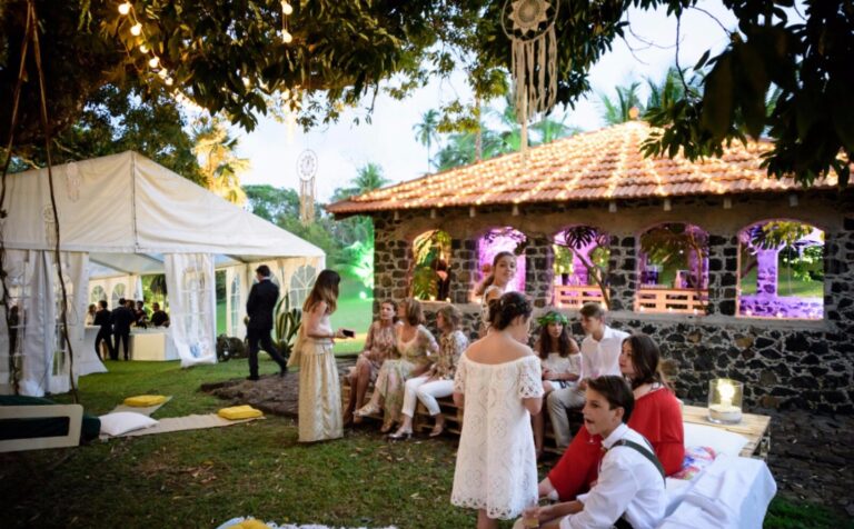 Guests gathered by a white marquee and a stone pavilion in a shaded garden, Myl'Evasions