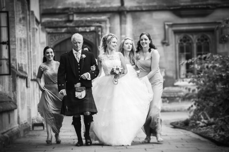 A bride walking in with her father and two bridesmaids, stone archway behind them, Nadine Pyke Make Up Artist