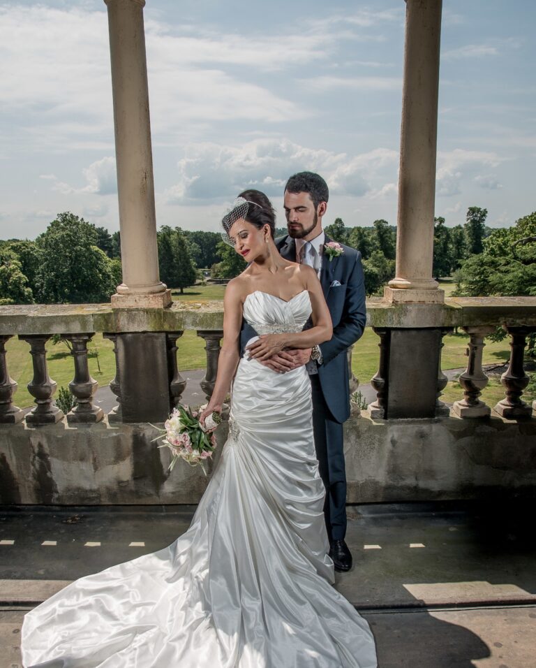 A bride and groom on a stone balustraded balcony overlooking the grounds, Nadine Pyke Make Up Artist