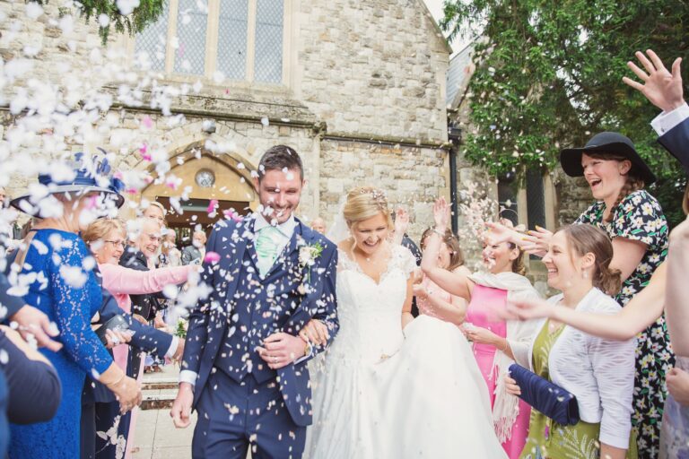 A bride and groom walking through confetti outside a stone church, Nadine Pyke Make Up Artist