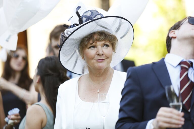 A wedding guest in a wide-brimmed hat, champagne in hand, Nadine Pyke Make Up Artist