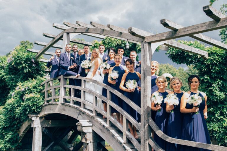 A wedding party gathered on a wooden bridge, navy bridesmaid dresses, Nadine Pyke Make Up Artist
