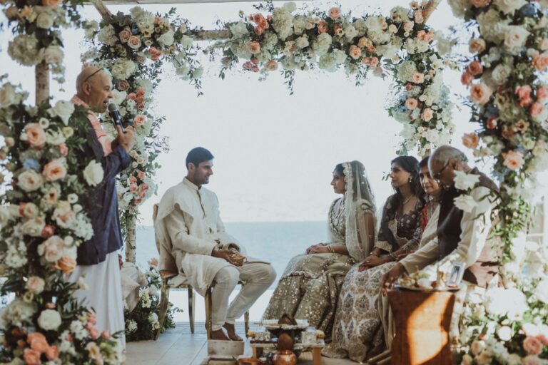 Couple and family seated beneath a flower arch above the sea, Naido Wedding