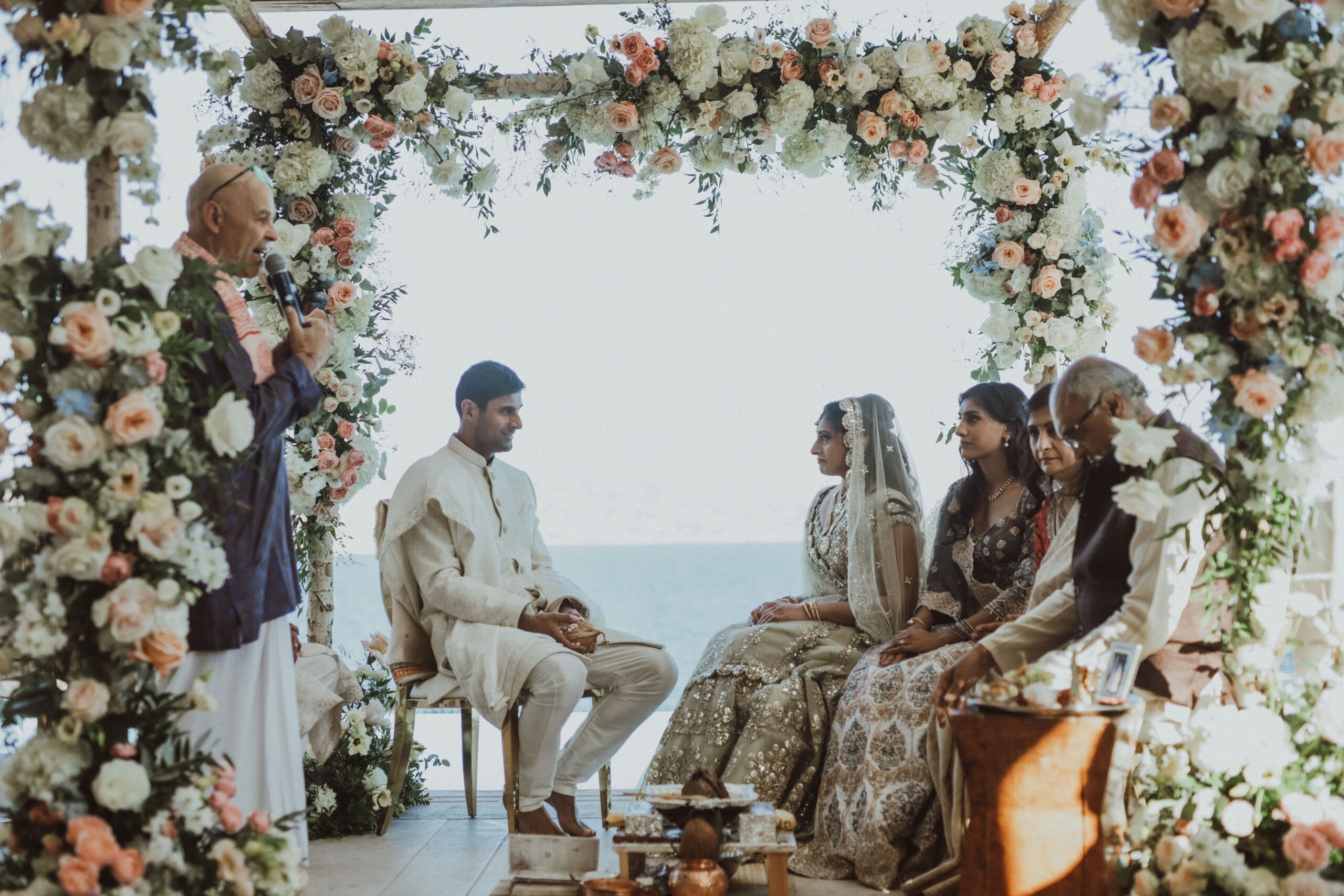 Couple and family seated beneath a flower arch above the sea, Naido Wedding