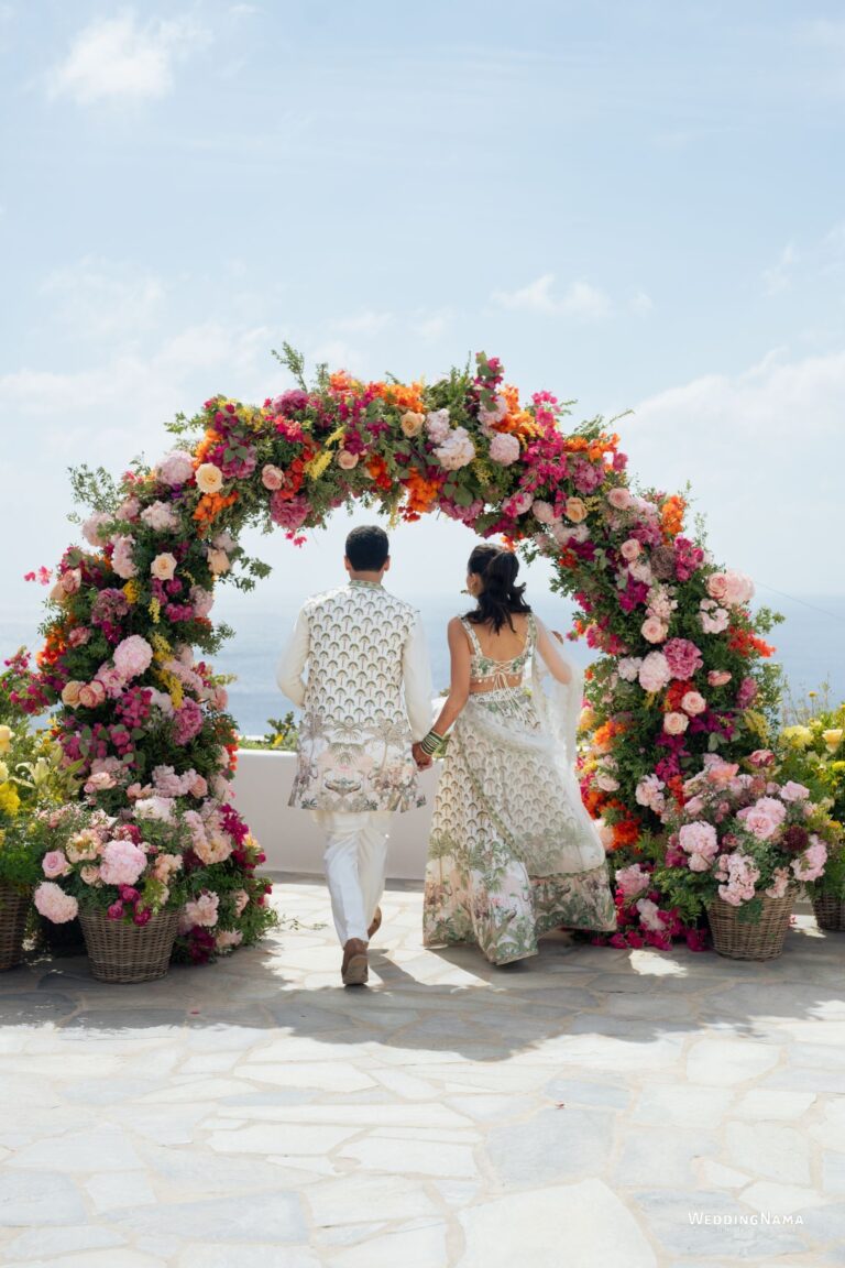 Couple walking toward a floral arch in pink, orange and yellow, Naido Wedding