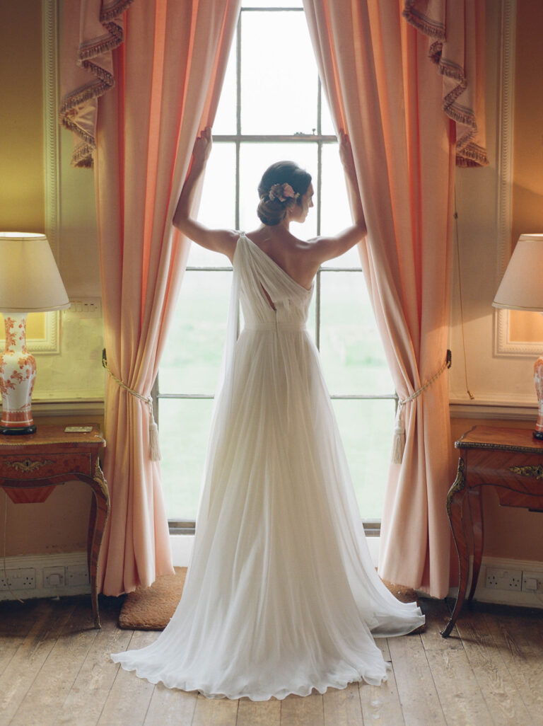 A bride in a Naomi Neoh gown at a tall window, Delicately Decadent styled shoot