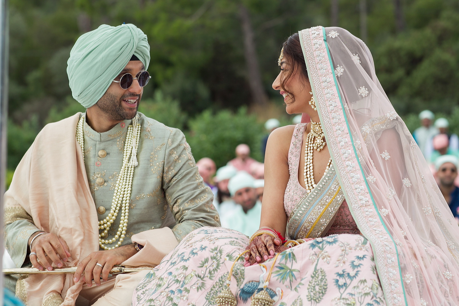 Bride and groom seated together during an Indian wedding ceremony, guests behind, Nilyum Wedding and Event Design