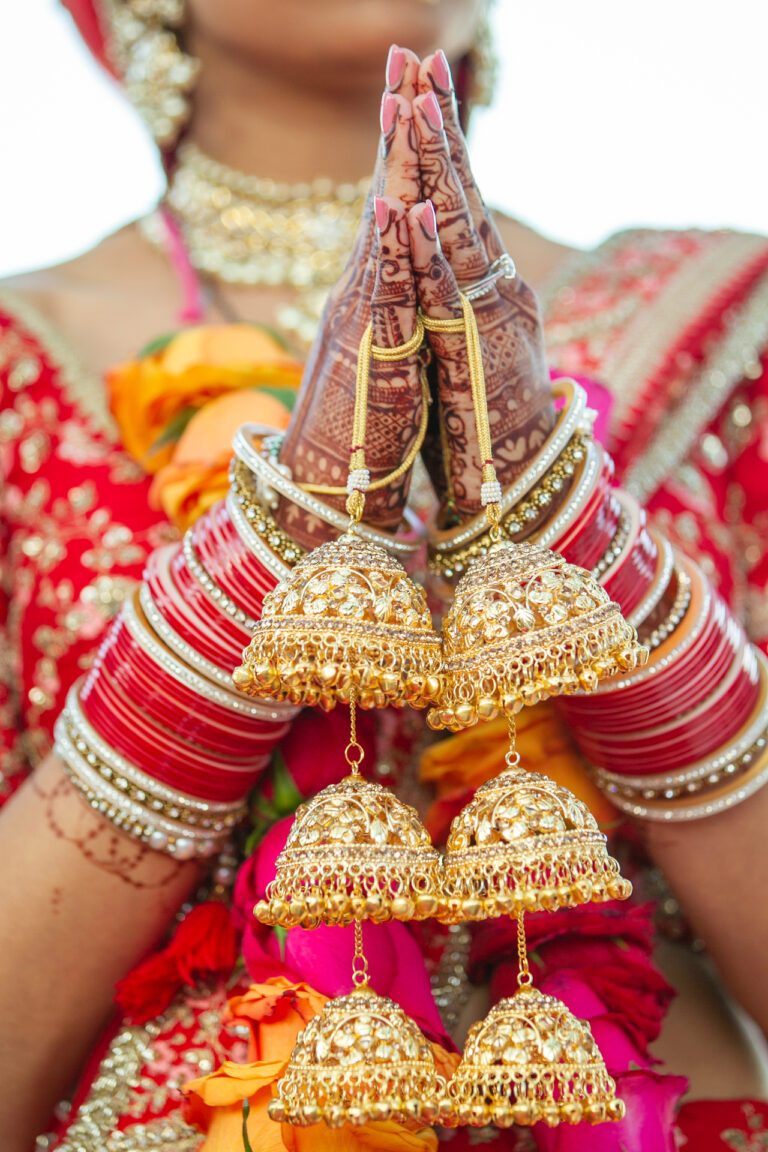 Bride's hands in prayer with gold jhumka earrings and red bangles, Nilyum Wedding and Event Design
