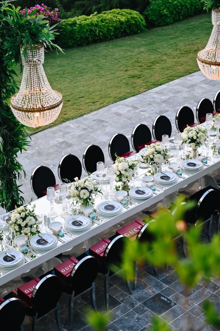 Long banquet table with floral runner beneath hanging chandeliers, Nilyum Wedding and Event Design