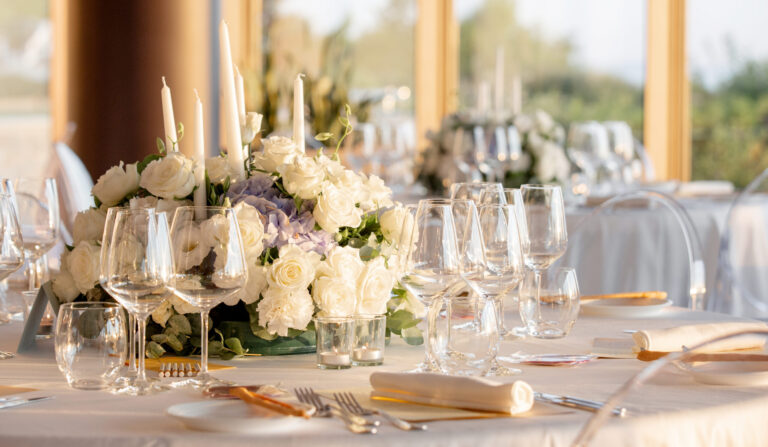 A round table with white roses, hydrangea and tall candles in a glass-walled room, Noemi Wedding
