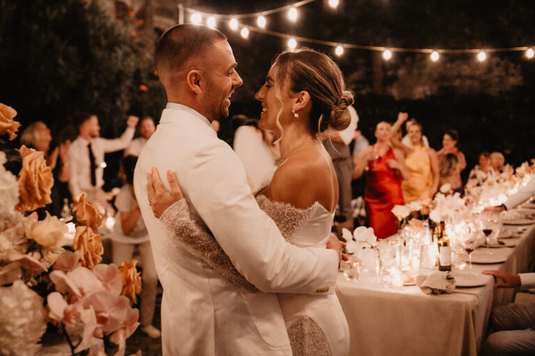 The first dance beside the long table under festoon lights, guests on their feet, Noemi Wedding