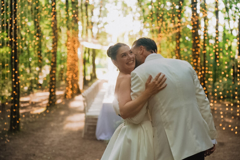 An avenue of trees hung with strings of lights, the couple embracing at the end of it, Noemi Wedding