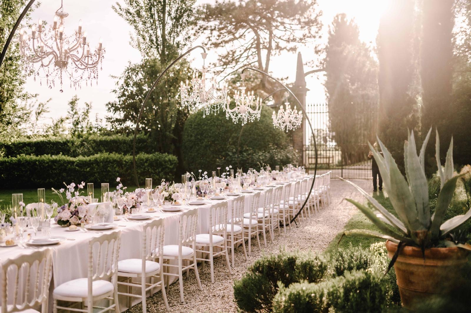 A long table in a formal garden under suspended crystal chandeliers, agave in a terracotta pot beside the gravel, Noemi Wedding