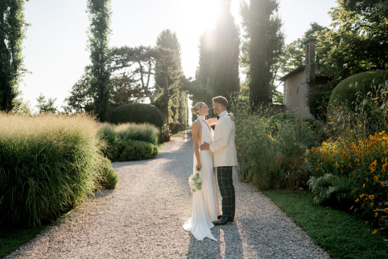 A couple on a gravel path between cypresses and ornamental grasses in a villa garden, Noemi Wedding