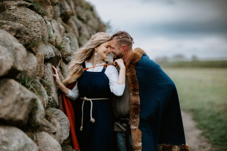 Couple in Viking-style costume beside a stone wall, Nordic Adventure Weddings