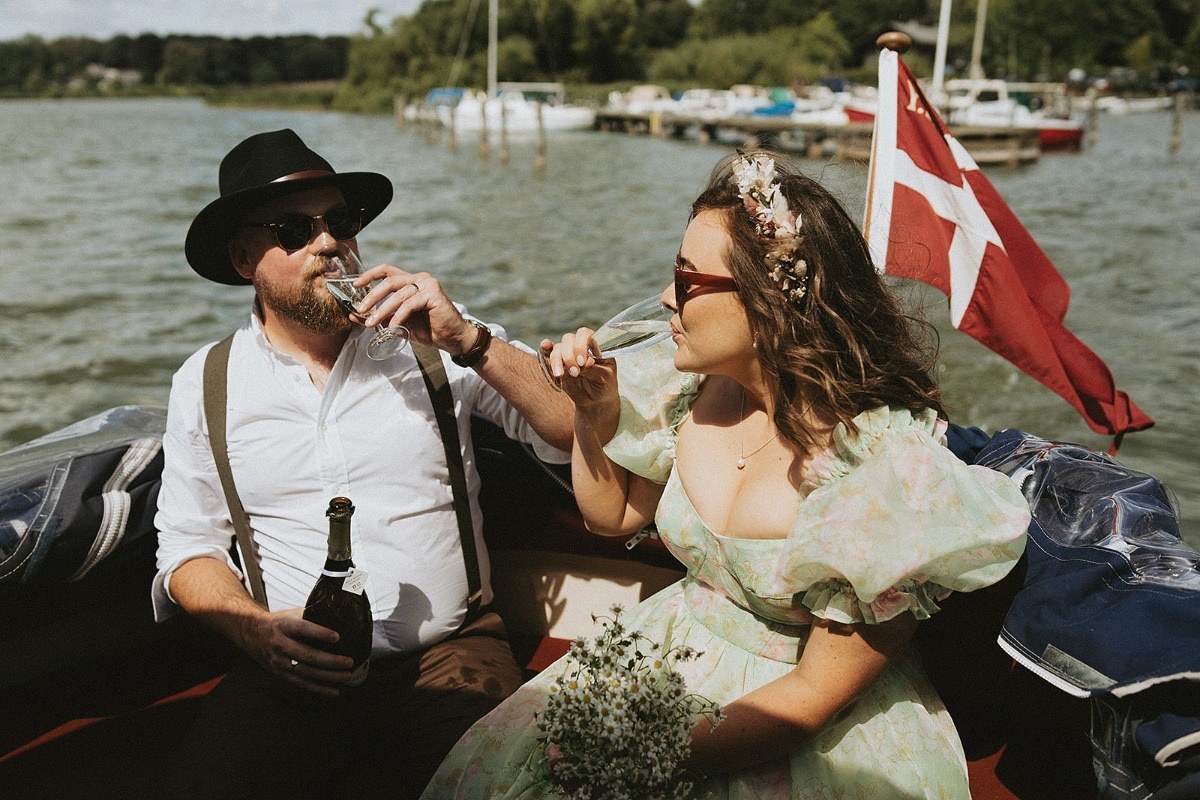 Couple toasting in a small boat flying the Danish flag, Nordic Adventure Weddings