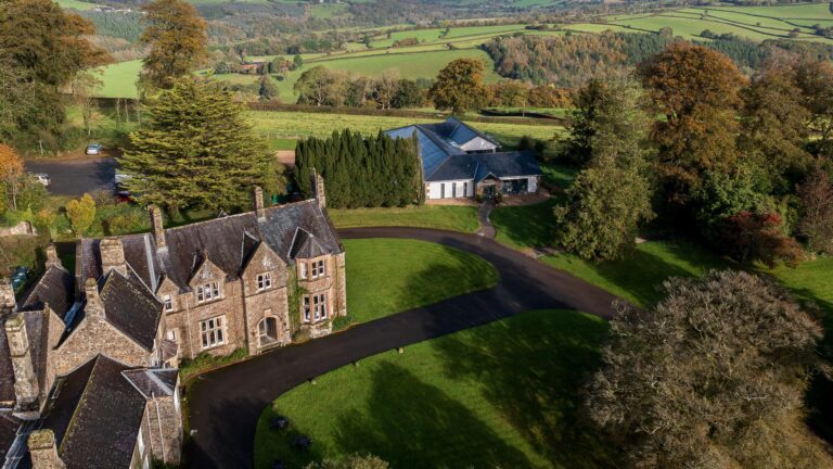 Aerial view of the manor roofs, the curving drive and lawns, with farmland of the Taw valley beyond, Northcote Manor Hotel