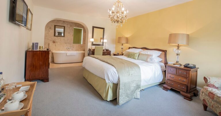 A bedroom with a freestanding bath set in an arched alcove beyond the bed, Northcote Manor Hotel