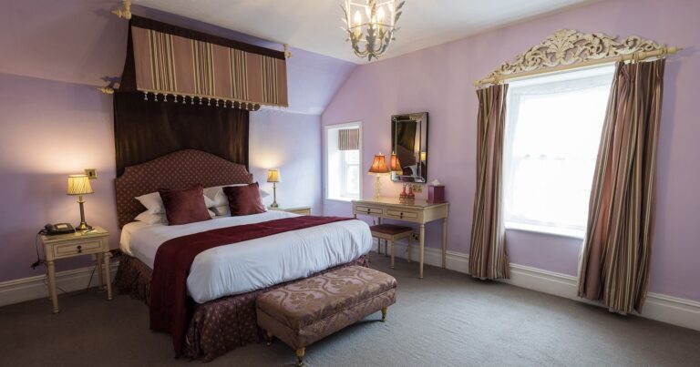A suite with a canopy over the bed, lilac walls and a tall window, Northcote Manor Hotel