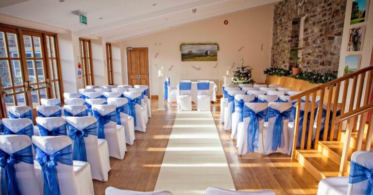 The conservatory laid out for a ceremony, with white chair covers tied with blue sashes either side of an aisle, Northcote Manor Hotel