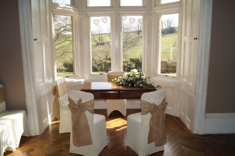 A ceremony table with flowers set in a tall bay window looking out to green fields, Northcote Manor Hotel